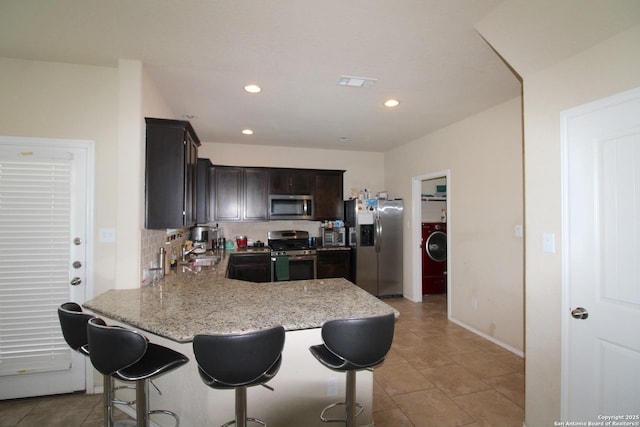 kitchen featuring sink, backsplash, stainless steel appliances, light stone countertops, and dark brown cabinets