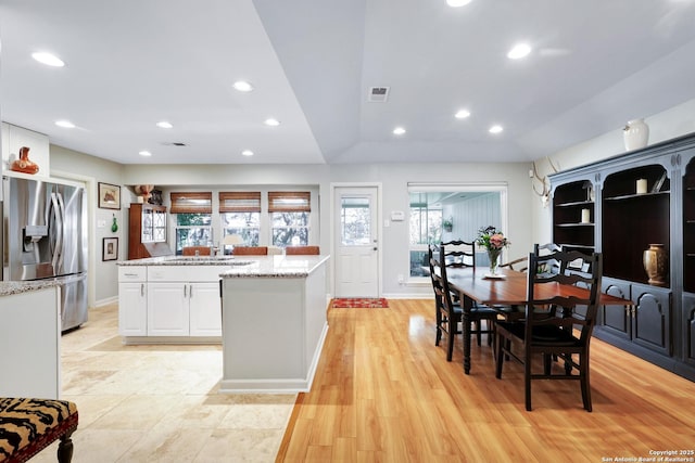 kitchen featuring white cabinets, a center island, stainless steel fridge with ice dispenser, light stone countertops, and light wood-type flooring