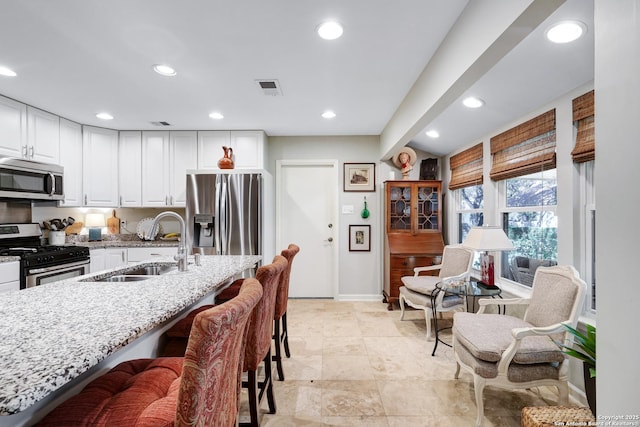 kitchen featuring a breakfast bar, sink, white cabinetry, light stone counters, and stainless steel appliances