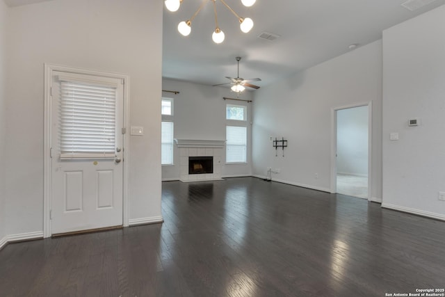 unfurnished living room featuring dark wood-type flooring, a tiled fireplace, and ceiling fan with notable chandelier