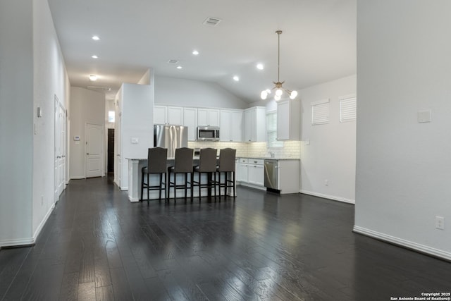 kitchen with dark wood-type flooring, appliances with stainless steel finishes, hanging light fixtures, tasteful backsplash, and white cabinets