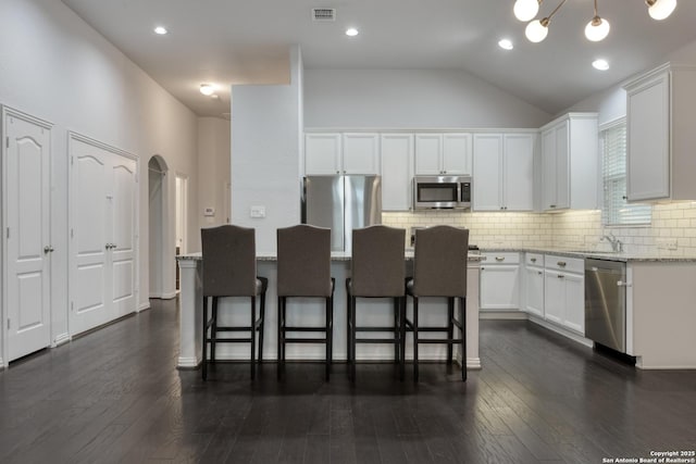 kitchen with appliances with stainless steel finishes, light stone counters, white cabinets, a kitchen bar, and decorative backsplash