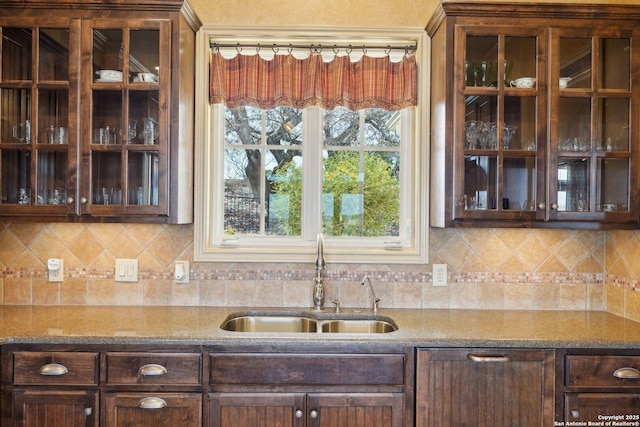 kitchen with dark brown cabinetry, sink, backsplash, and dark stone countertops