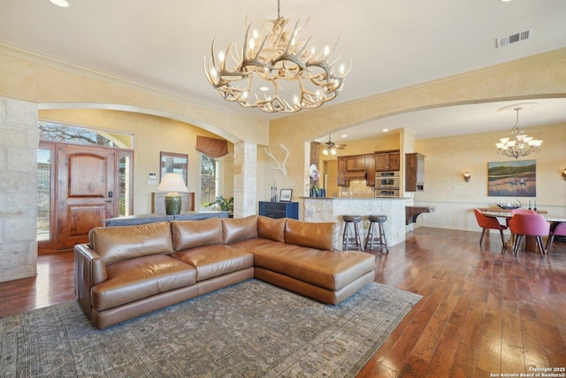 living room with crown molding, dark wood-type flooring, and ceiling fan with notable chandelier