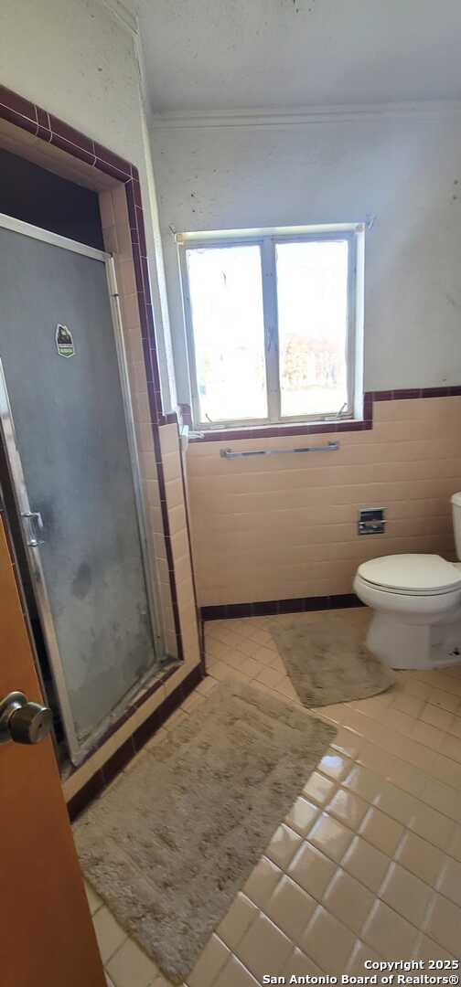 bathroom featuring tile walls, toilet, walk in shower, crown molding, and tile patterned floors