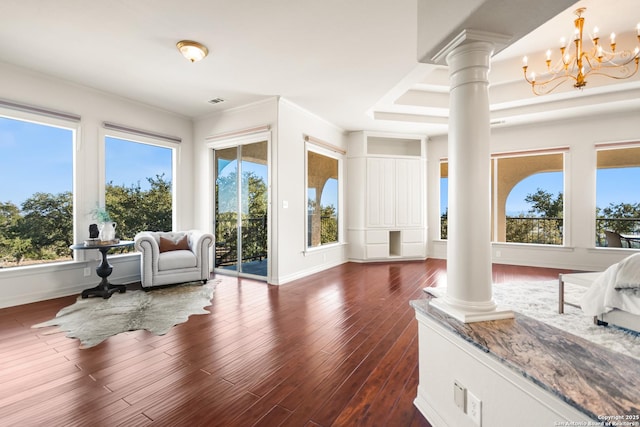 interior space featuring decorative columns, crown molding, dark wood-type flooring, and a notable chandelier