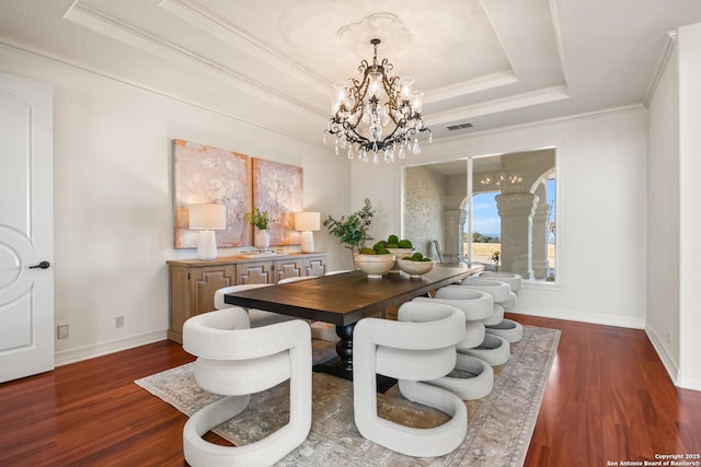 dining area with dark wood-type flooring, ornamental molding, a raised ceiling, and a chandelier