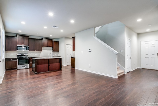 kitchen with dark wood-type flooring, appliances with stainless steel finishes, backsplash, an island with sink, and a kitchen bar