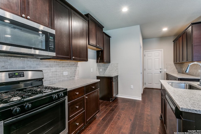 kitchen featuring dark wood-type flooring, sink, light stone counters, dark brown cabinets, and stainless steel appliances