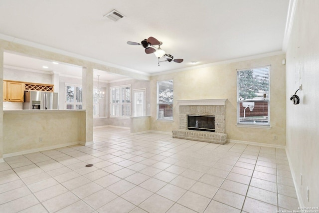 unfurnished living room with plenty of natural light, ceiling fan with notable chandelier, a brick fireplace, and light tile patterned floors