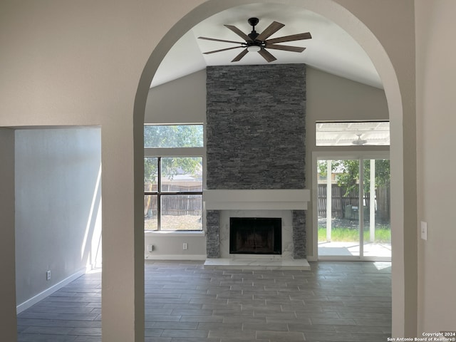 unfurnished living room with ceiling fan, lofted ceiling, a stone fireplace, and dark hardwood / wood-style flooring