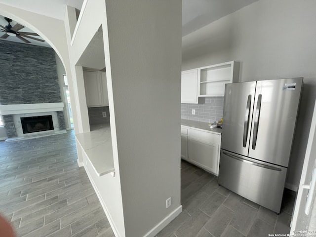 kitchen with tasteful backsplash, white cabinetry, a large fireplace, stainless steel fridge, and ceiling fan