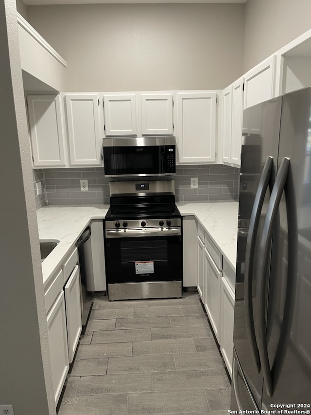 kitchen with stainless steel appliances, light stone countertops, decorative backsplash, and white cabinets