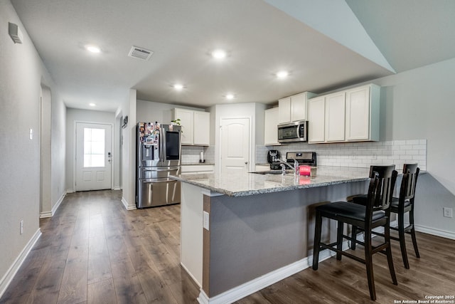 kitchen featuring a breakfast bar area, stainless steel appliances, white cabinets, dark hardwood / wood-style flooring, and kitchen peninsula