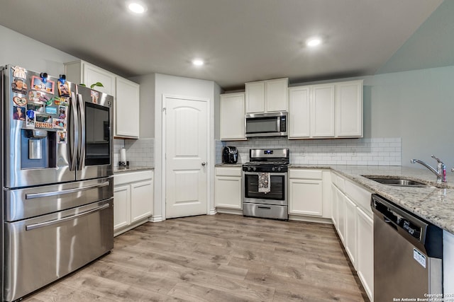 kitchen with sink, light hardwood / wood-style flooring, appliances with stainless steel finishes, light stone counters, and white cabinets