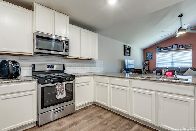 kitchen with vaulted ceiling, appliances with stainless steel finishes, white cabinets, light hardwood / wood-style floors, and kitchen peninsula