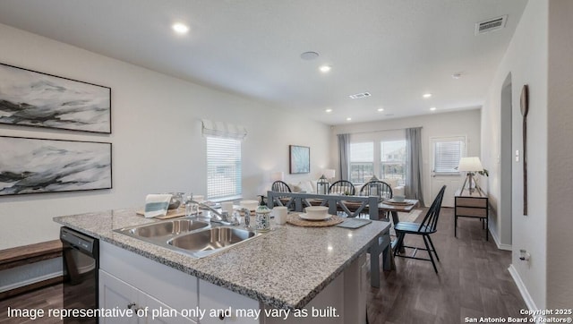 kitchen featuring sink, dishwasher, white cabinetry, light stone counters, and a center island with sink