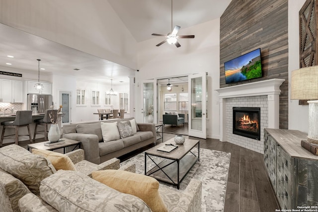 living room featuring ceiling fan, a tiled fireplace, dark wood-type flooring, and a towering ceiling