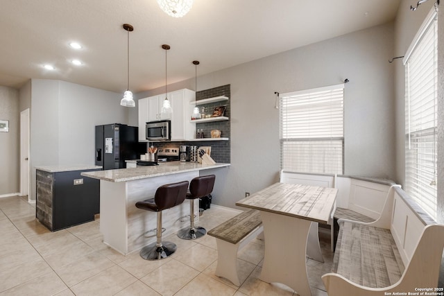 kitchen with white cabinetry, decorative light fixtures, kitchen peninsula, stainless steel appliances, and light stone countertops