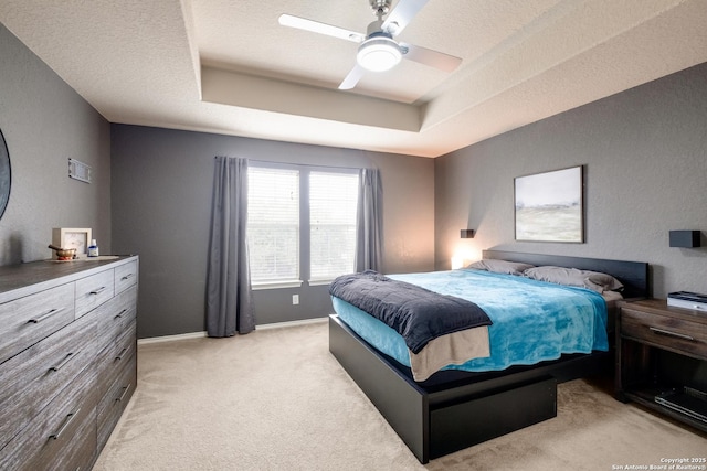 bedroom with ceiling fan, light carpet, a textured ceiling, and a tray ceiling