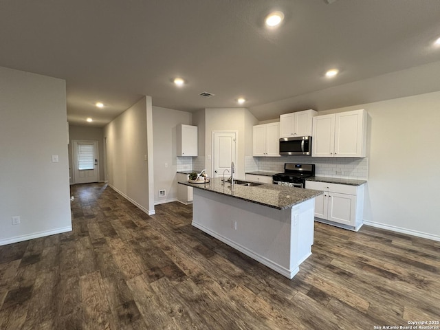 kitchen with sink, white cabinetry, a kitchen island with sink, stainless steel appliances, and dark stone counters