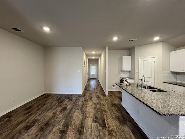 kitchen featuring dark wood-type flooring, sink, dark stone countertops, an island with sink, and white cabinets