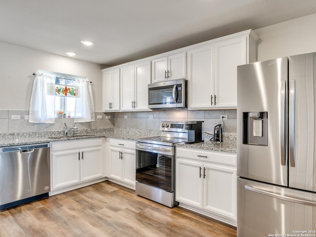 kitchen featuring sink, white cabinetry, light wood-type flooring, appliances with stainless steel finishes, and decorative backsplash