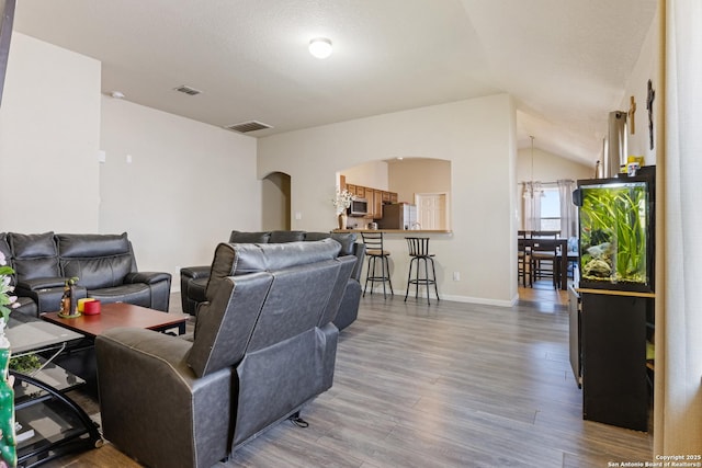 living room featuring hardwood / wood-style flooring, vaulted ceiling, and a notable chandelier