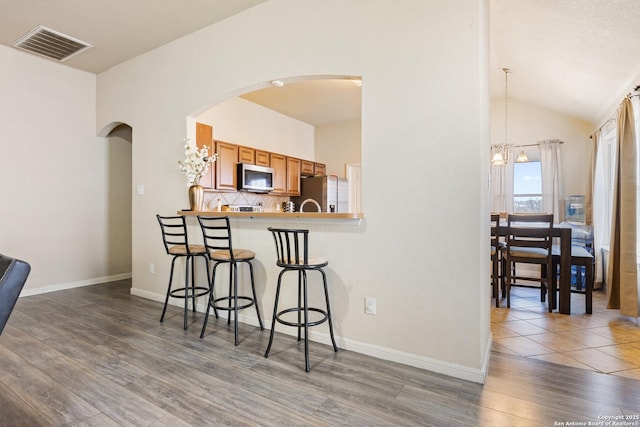 kitchen with appliances with stainless steel finishes, tasteful backsplash, a breakfast bar area, kitchen peninsula, and dark wood-type flooring