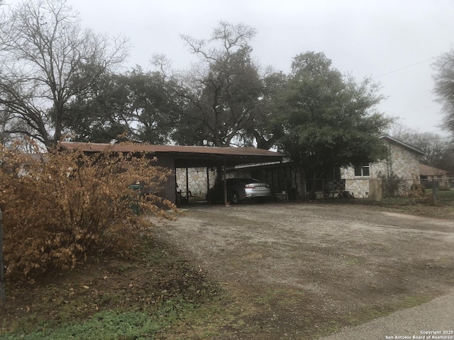 exterior space with dirt driveway, a carport, and fence