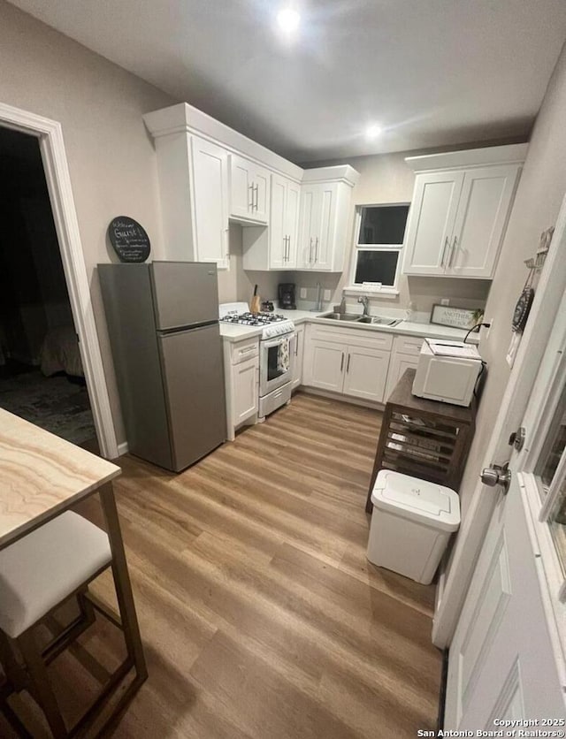 kitchen with stainless steel refrigerator, white cabinetry, white gas range, and light hardwood / wood-style flooring