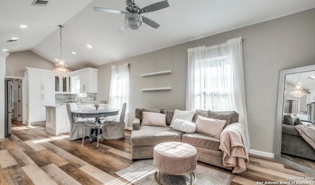 living room featuring vaulted ceiling, ceiling fan with notable chandelier, and light hardwood / wood-style floors