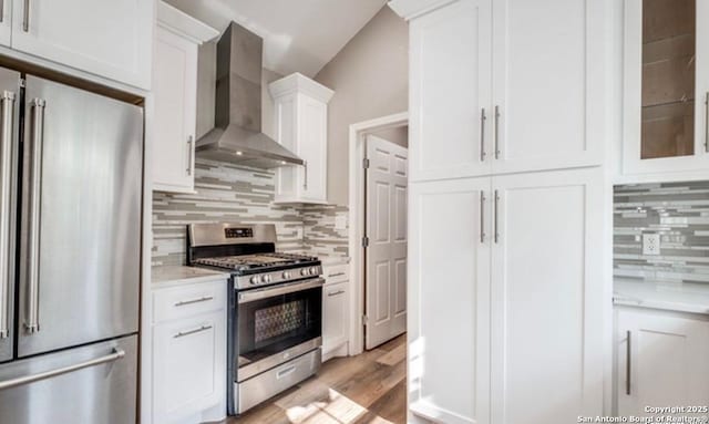 kitchen featuring appliances with stainless steel finishes, tasteful backsplash, white cabinets, light wood-type flooring, and wall chimney exhaust hood