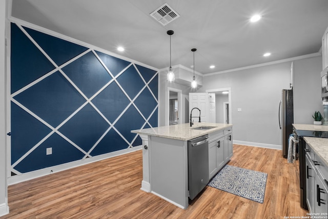 kitchen featuring appliances with stainless steel finishes, decorative light fixtures, sink, light hardwood / wood-style floors, and a center island with sink