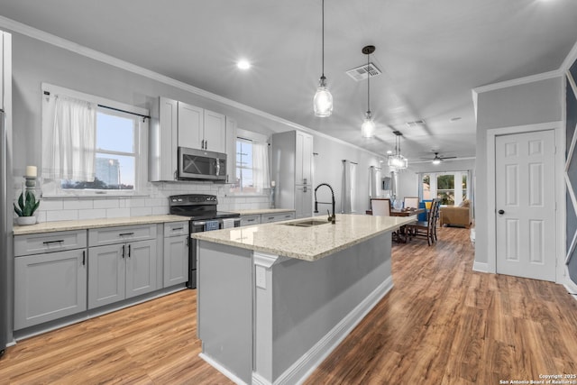 kitchen with appliances with stainless steel finishes, an island with sink, sink, hanging light fixtures, and light stone counters