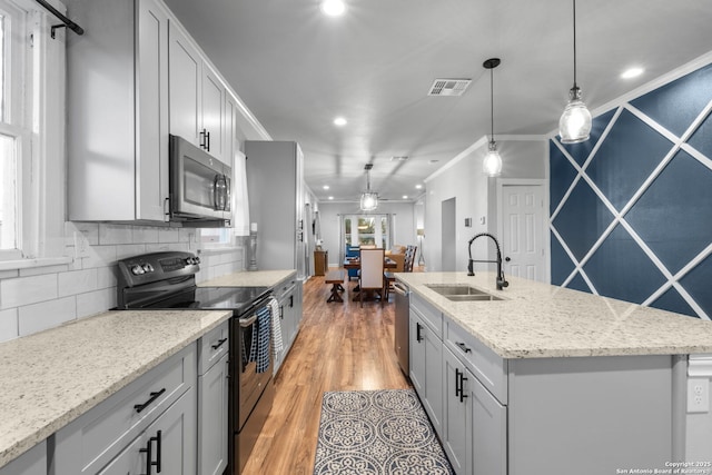 kitchen with pendant lighting, sink, ornamental molding, stainless steel appliances, and a center island with sink