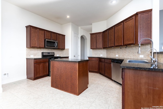 kitchen with sink, light tile patterned floors, appliances with stainless steel finishes, backsplash, and a kitchen island