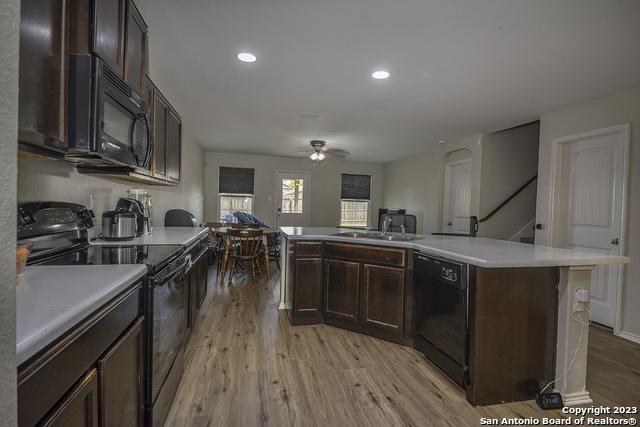 kitchen with sink, dark brown cabinets, a center island, black appliances, and light hardwood / wood-style floors