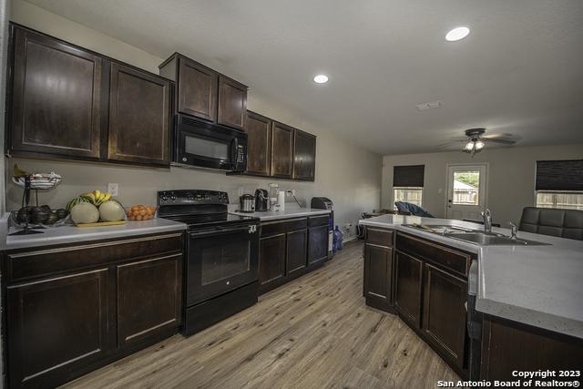 kitchen with sink, ceiling fan, black appliances, dark brown cabinets, and light hardwood / wood-style flooring