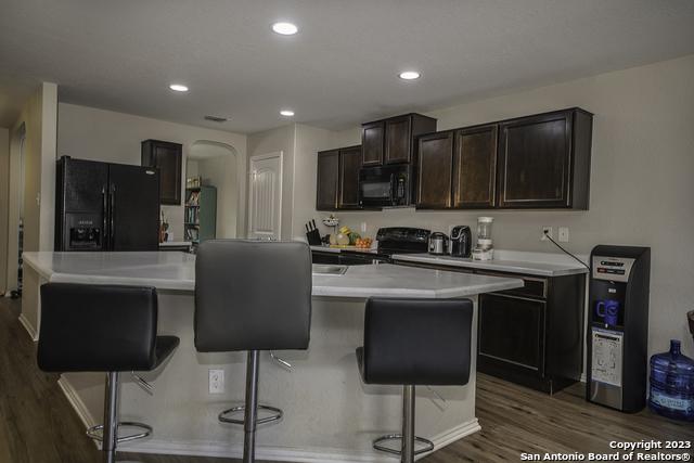 kitchen featuring a breakfast bar area, dark brown cabinets, dark hardwood / wood-style flooring, a kitchen island, and black appliances