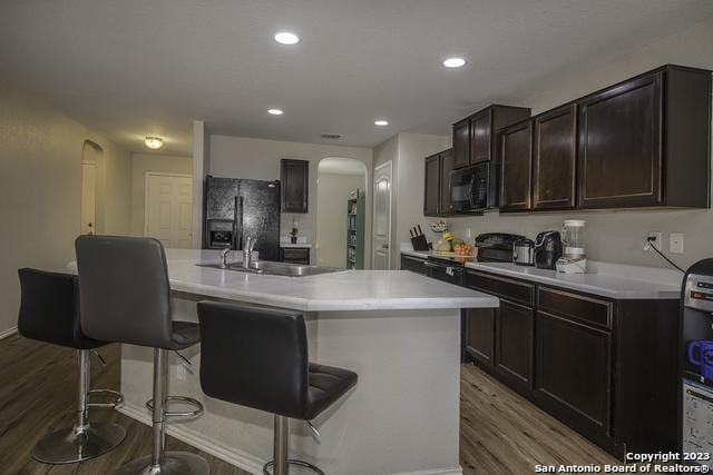 kitchen with sink, hardwood / wood-style flooring, a breakfast bar area, a kitchen island with sink, and black appliances