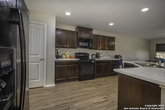 kitchen featuring sink, dark brown cabinets, black appliances, light hardwood / wood-style floors, and kitchen peninsula