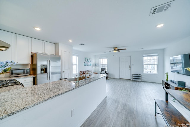 kitchen with appliances with stainless steel finishes, sink, white cabinets, light stone counters, and light wood-type flooring