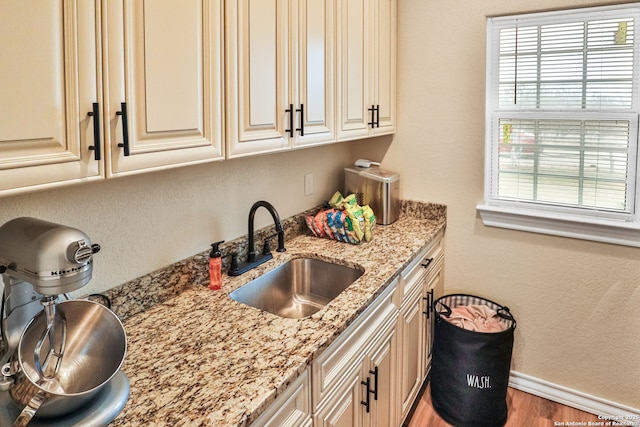 kitchen featuring hardwood / wood-style flooring, cream cabinets, sink, and light stone counters