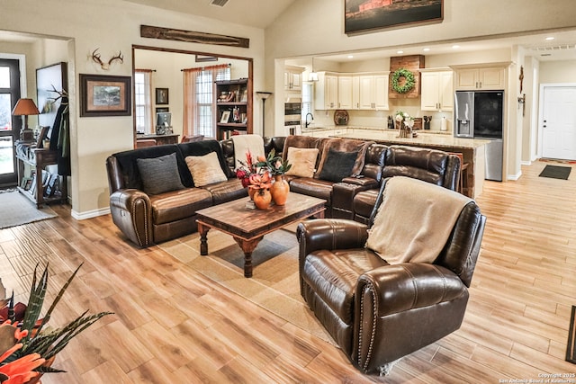 living room with high vaulted ceiling, sink, and light hardwood / wood-style flooring