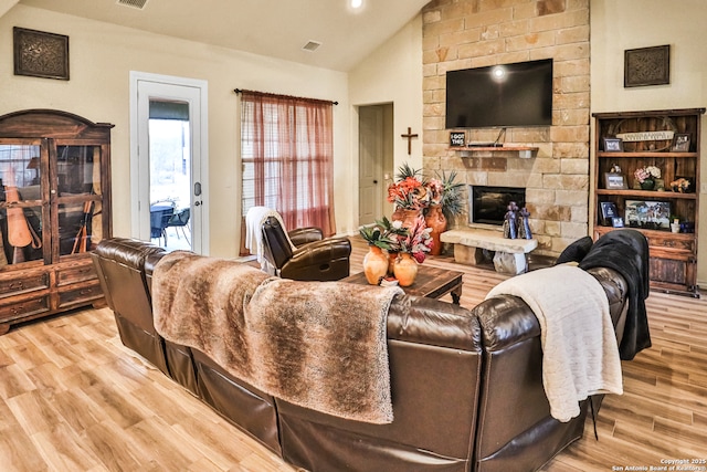 living room featuring lofted ceiling, a stone fireplace, and light hardwood / wood-style flooring