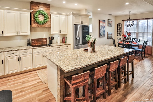 kitchen with pendant lighting, light stone counters, stainless steel fridge, and a center island