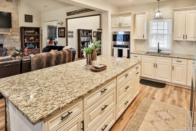 kitchen featuring sink, a stone fireplace, light stone counters, decorative light fixtures, and light wood-type flooring