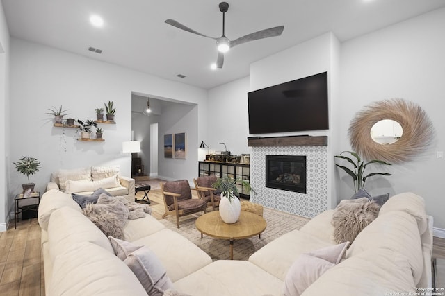 living room featuring ceiling fan, wood-type flooring, and a tile fireplace