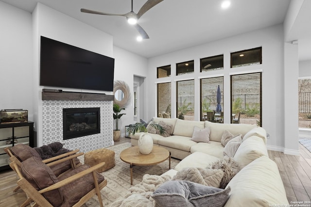 living room with ceiling fan, a fireplace, light hardwood / wood-style flooring, and a towering ceiling